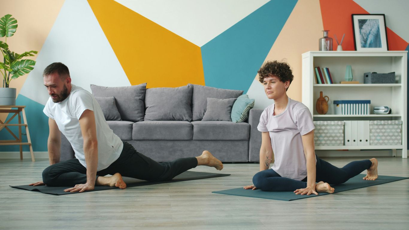 Couple doing yoga poses on mats in living room.