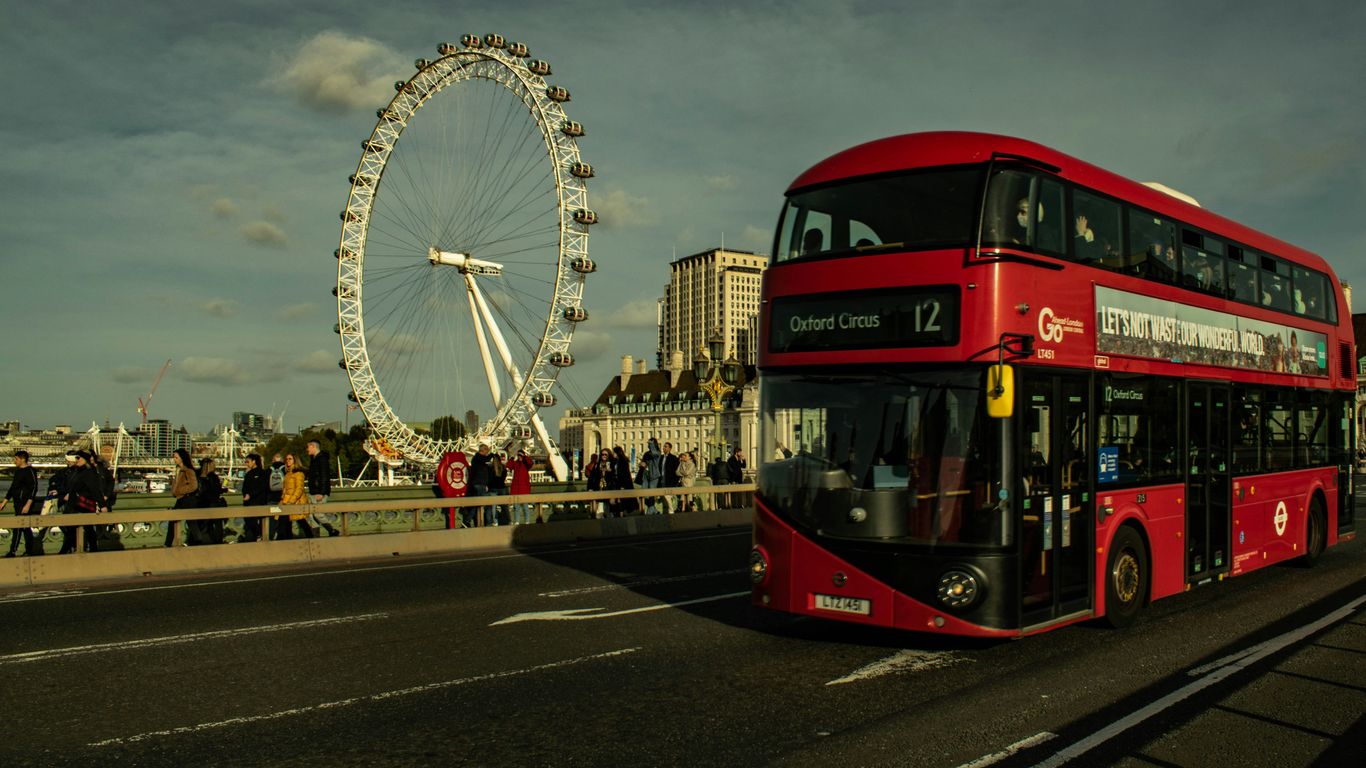 a red double decker bus driving past a ferris wheel