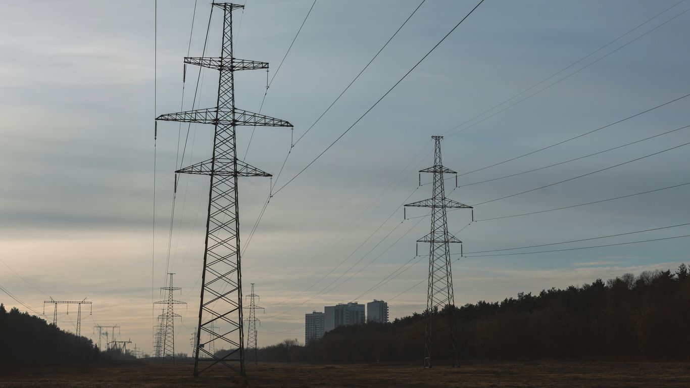 Power lines stretch across a field towards distant buildings.