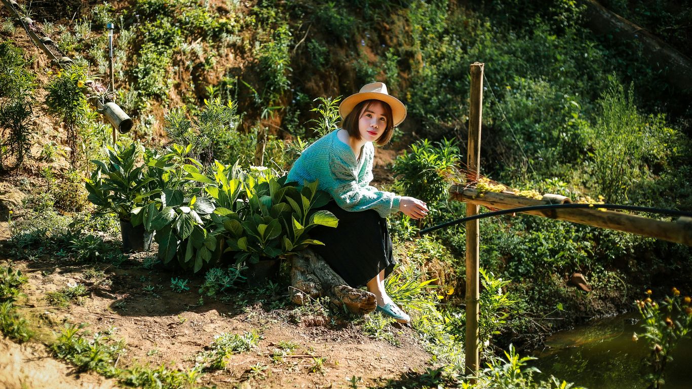 a woman in a hat is sitting on a tree stump