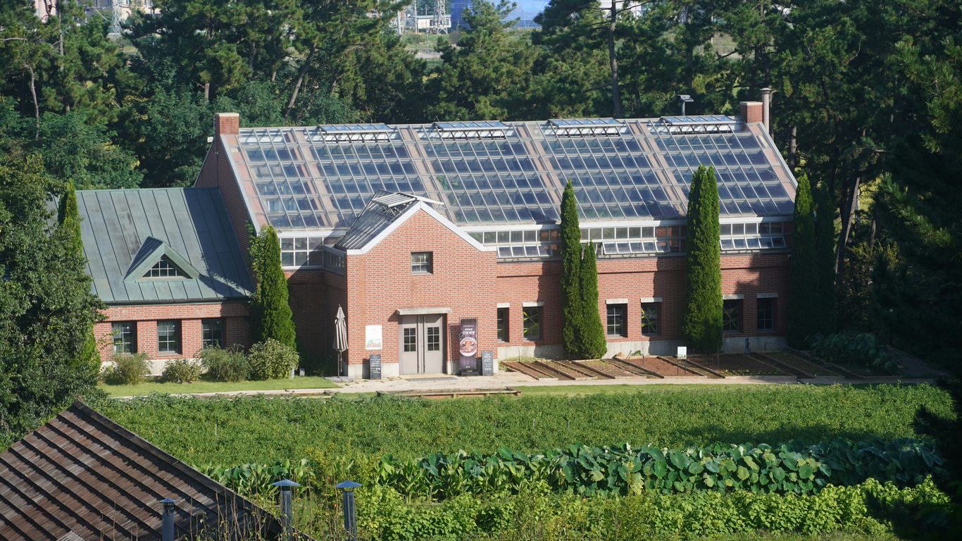 Brick building with a large glass roof surrounded by greenery.