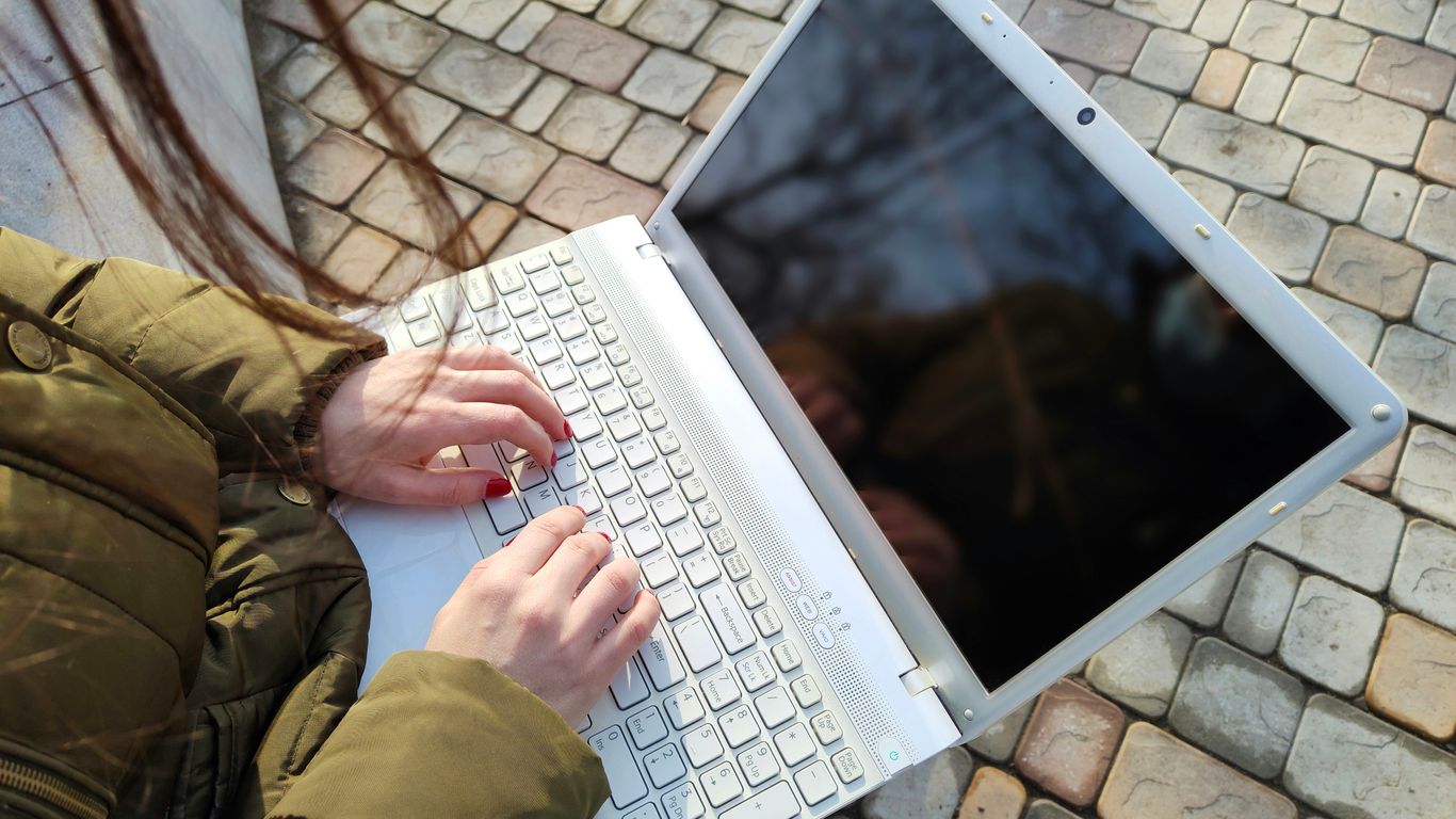 a woman is typing on a laptop outside
