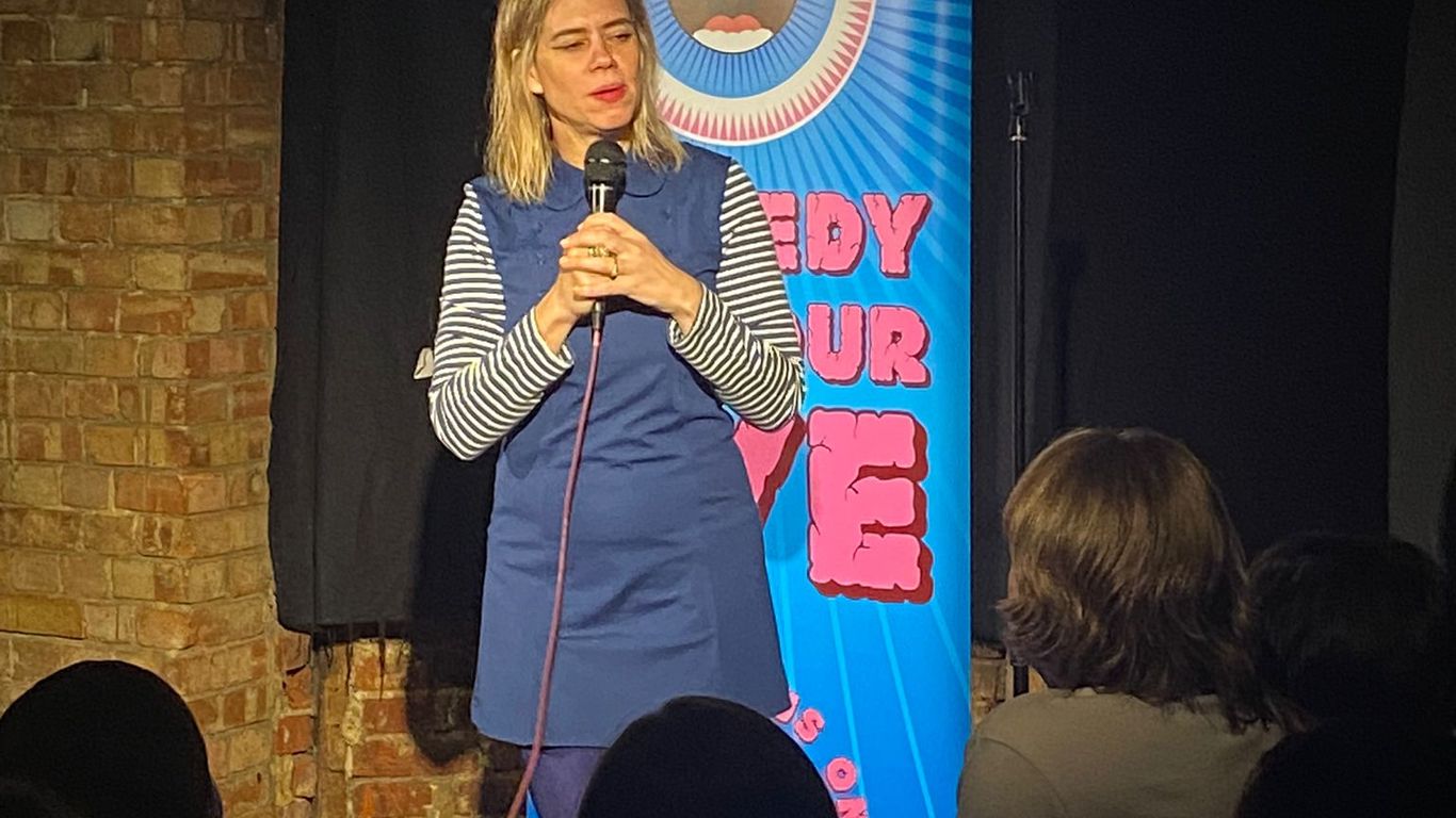 A comedian performs on stage in front of a banner.