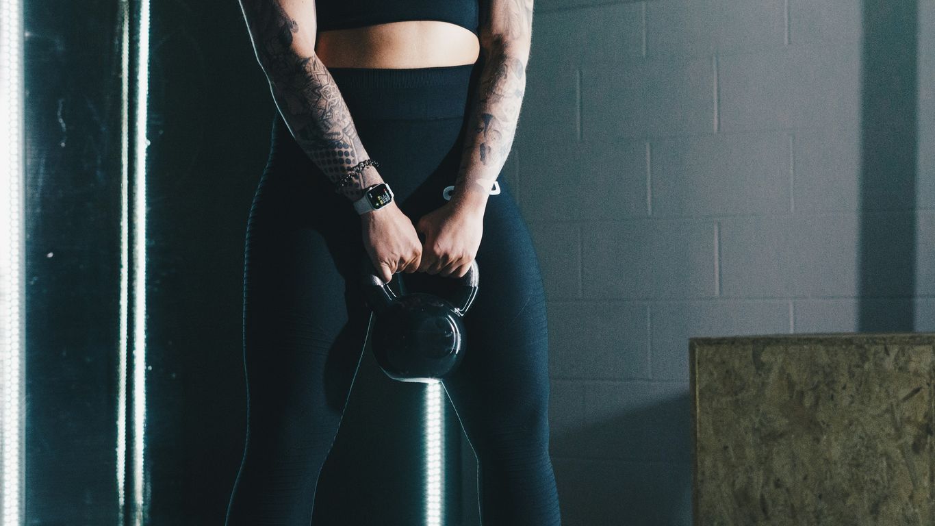 a woman with tattoos holding a kettle in a gym
