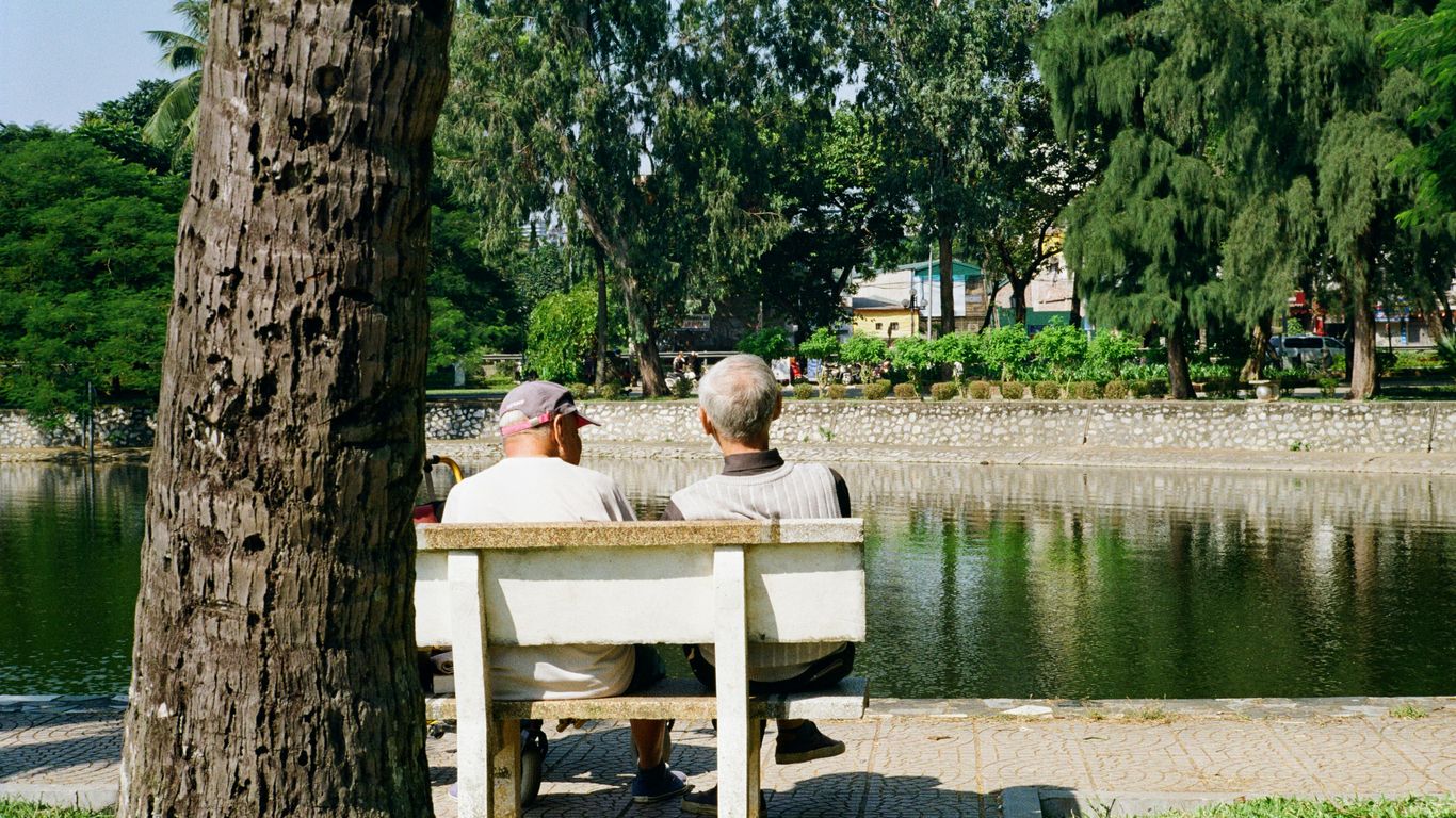 Two men sitting on a park bench by the water.