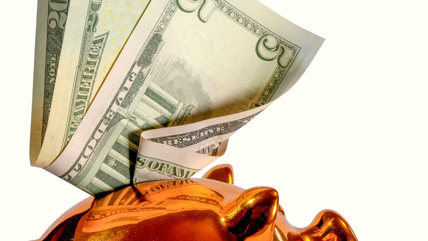 Us dollar bills being inserted into a piggy bank