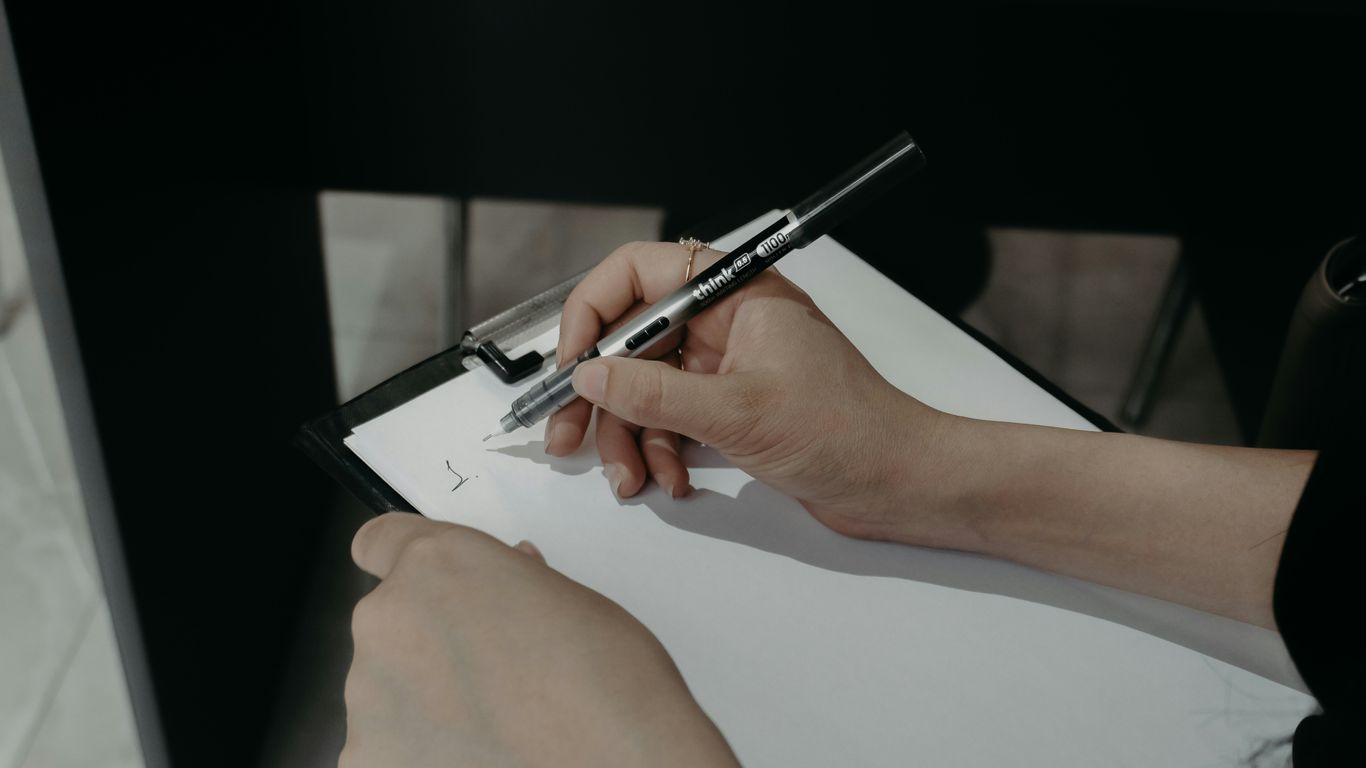 Hands writing on a clipboard with a pen.