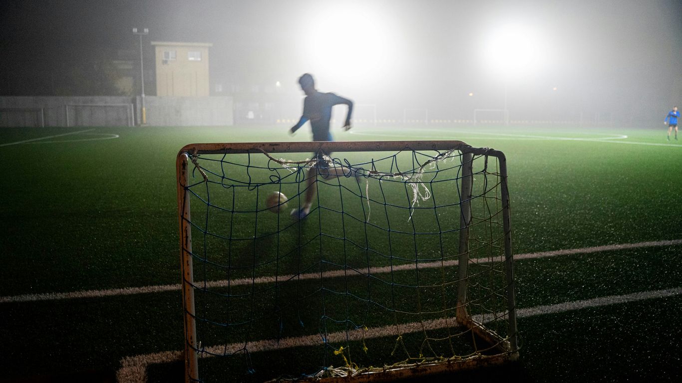 man in black shirt standing on soccer goal net during night time