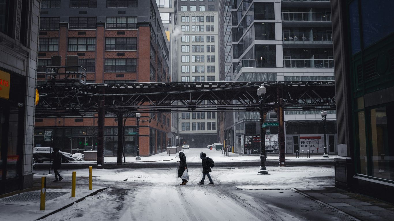 People cross a snowy street in a city.