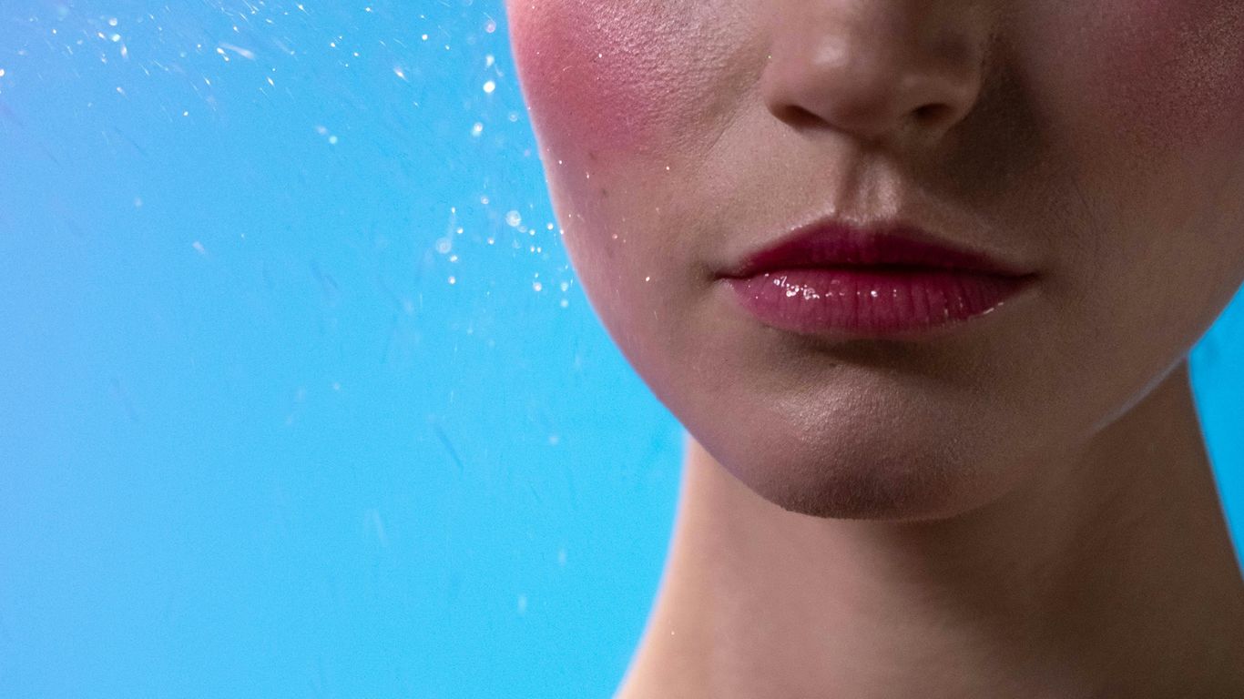 Person with closed eyes, colorful makeup, blue background, sparkles.