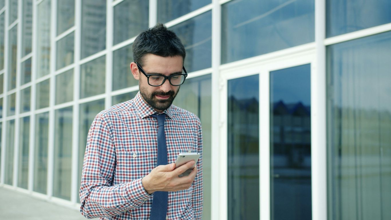 Man in glasses looking at his phone outside building
