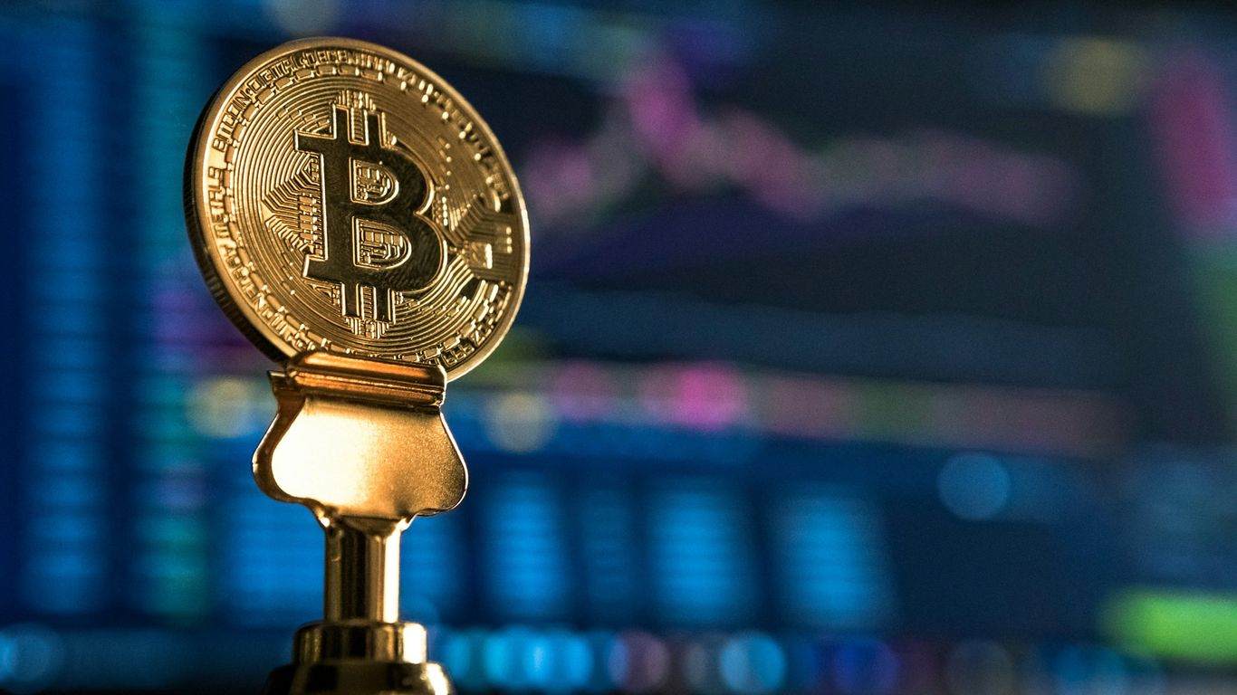 A gold Bitcoin replica with financial charts in the background.