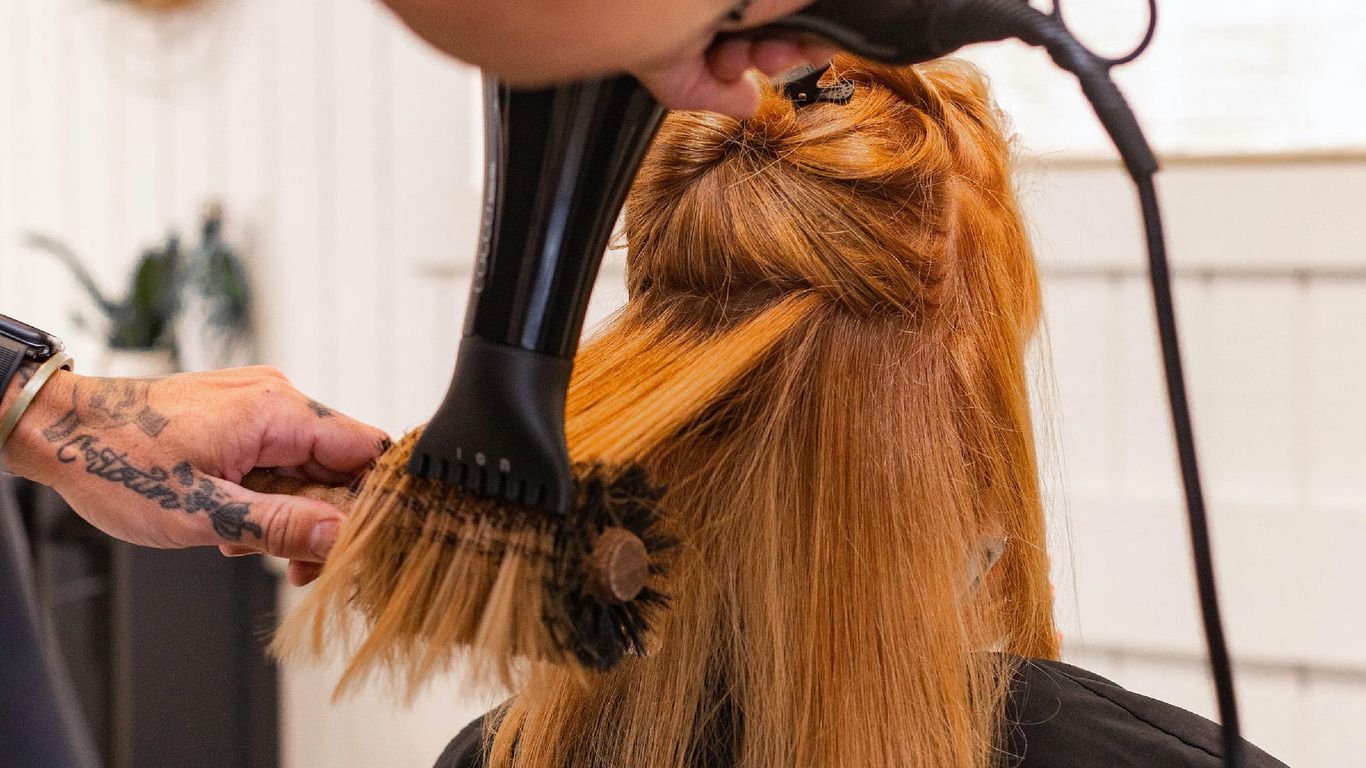 Hairdresser blow-drying client's hair in a salon.