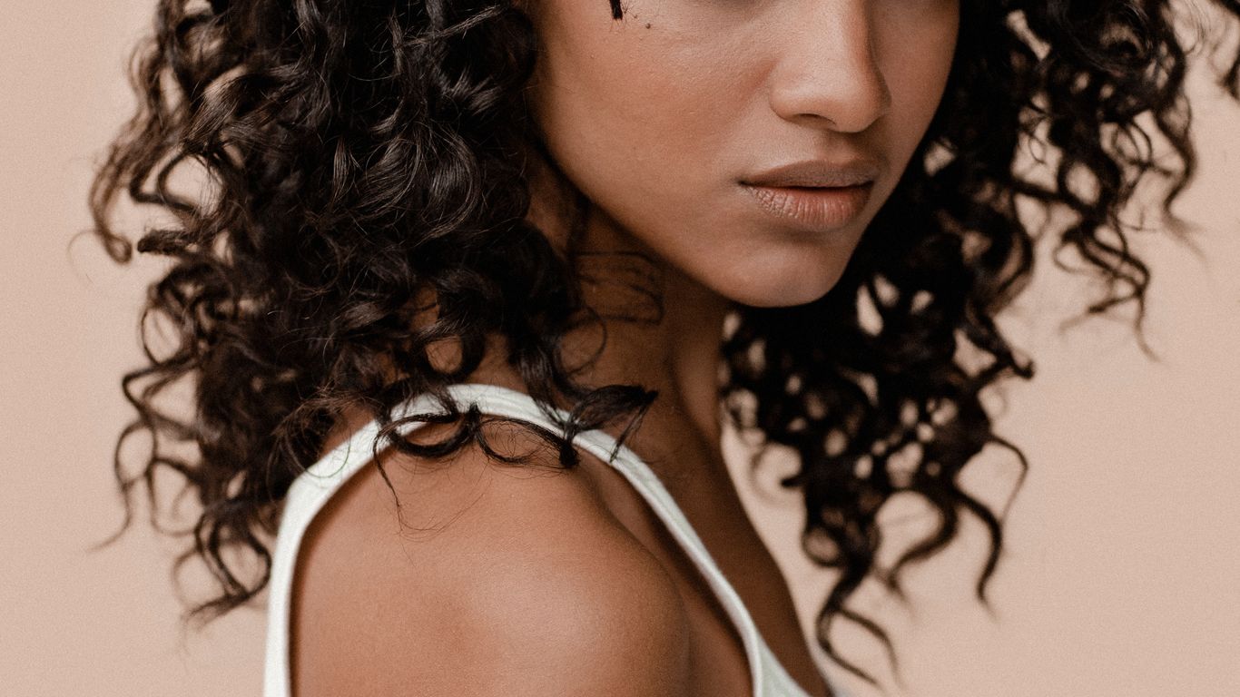 Curly-haired individual looking back over shoulder, neutral background, close-up.