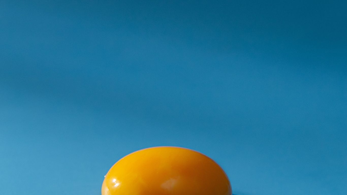 A single egg yolk on a blue background, casting shadow.