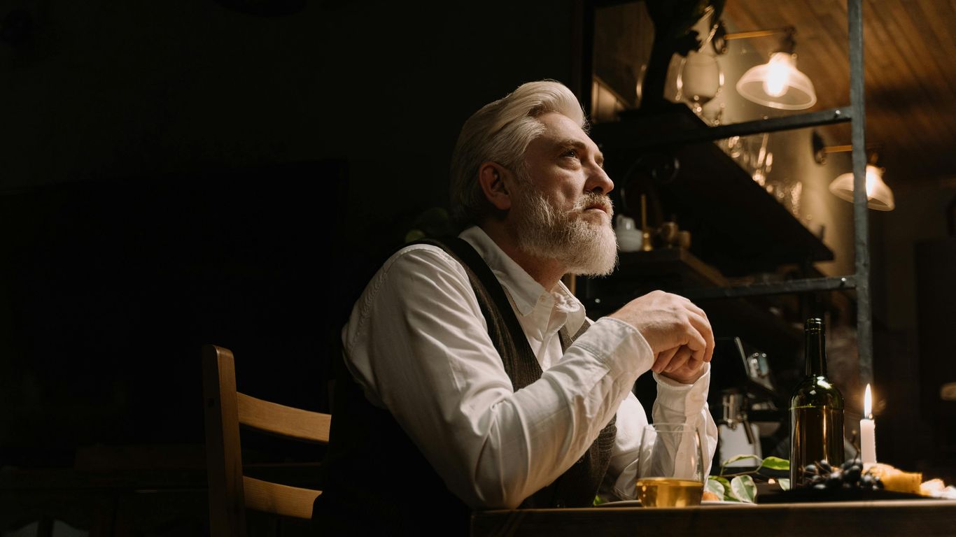 Person sitting at a table with wine, candle, thoughtful expression.