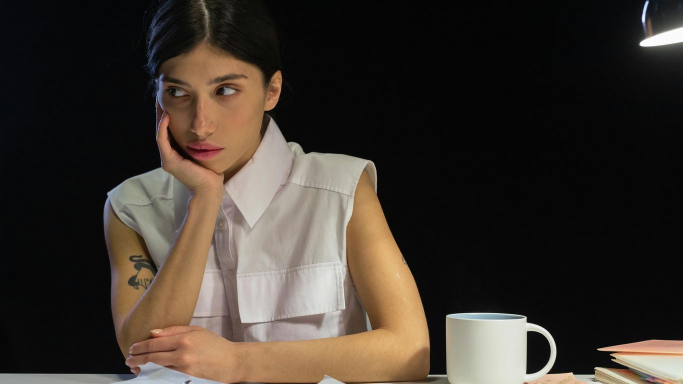 Person looking away from camera, resting chin on hand, with papers and mug.