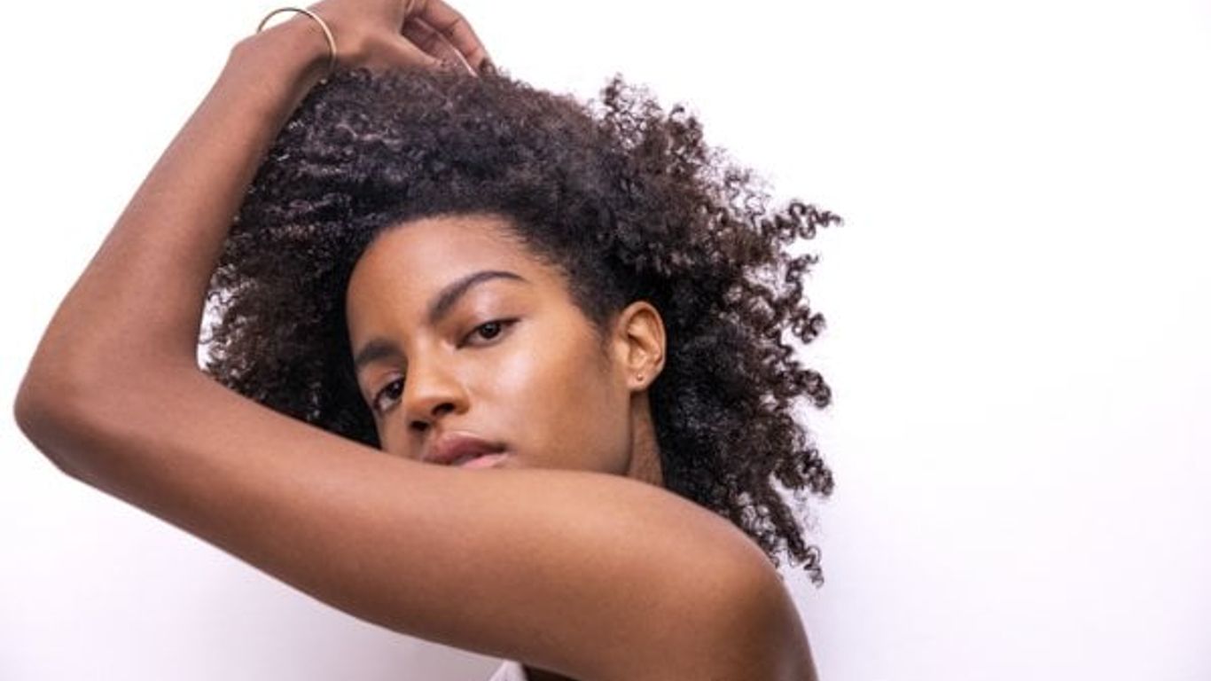 Woman posing gracefully, flaunting her natural curly hair, white background.