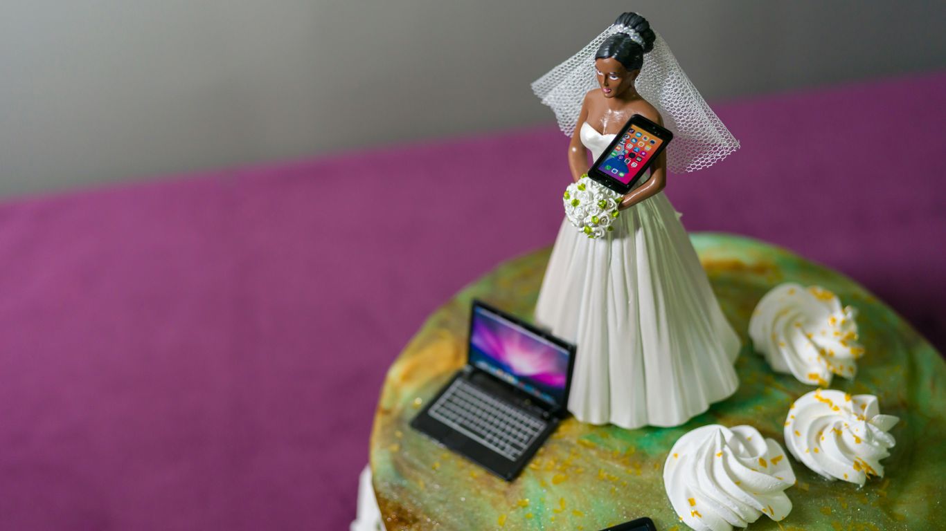 Bride cake topper holds tablet and laptop.