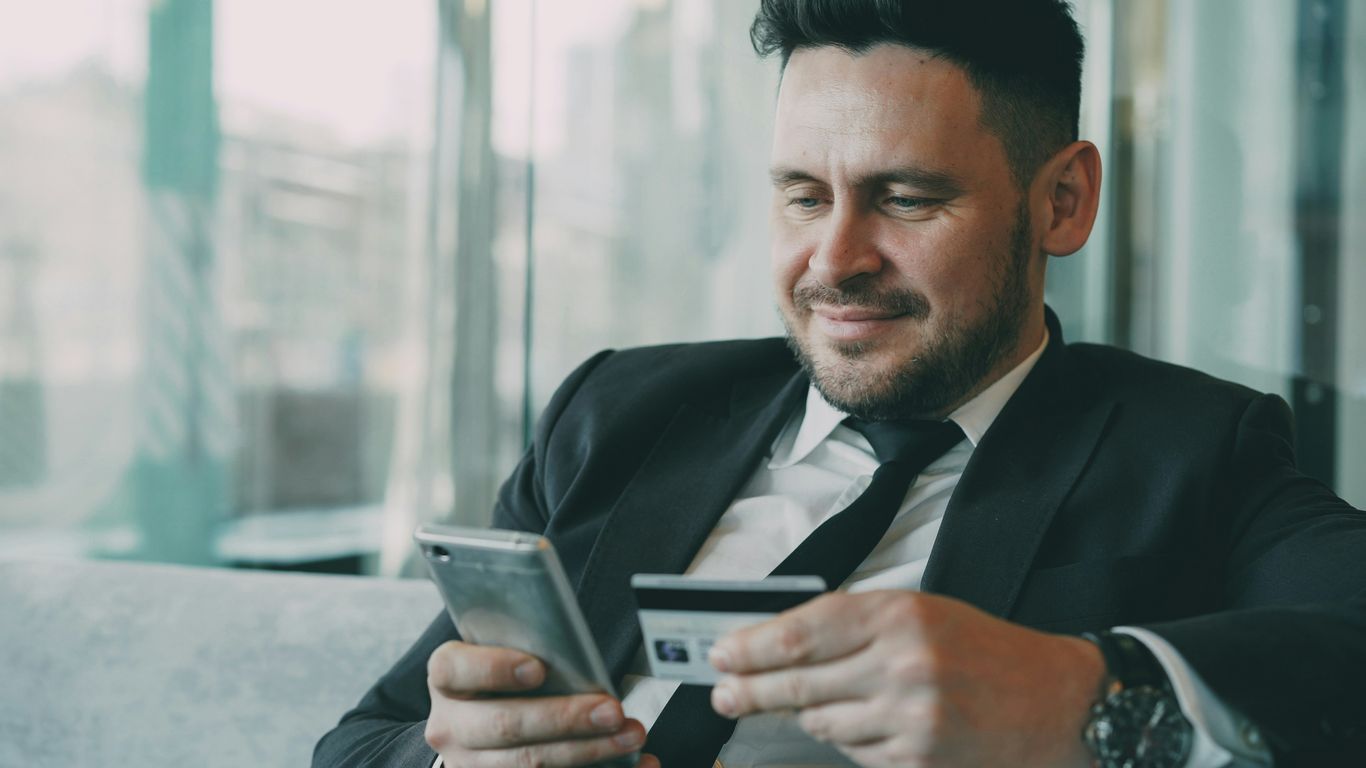 Man in suit using smartphone and credit card.