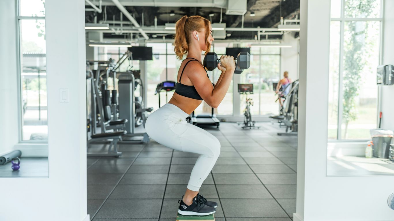 woman wearing black sports bra and white legging lifting dummbells