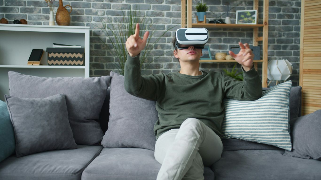 Man wearing vr headset sitting on sofa gesturing.
