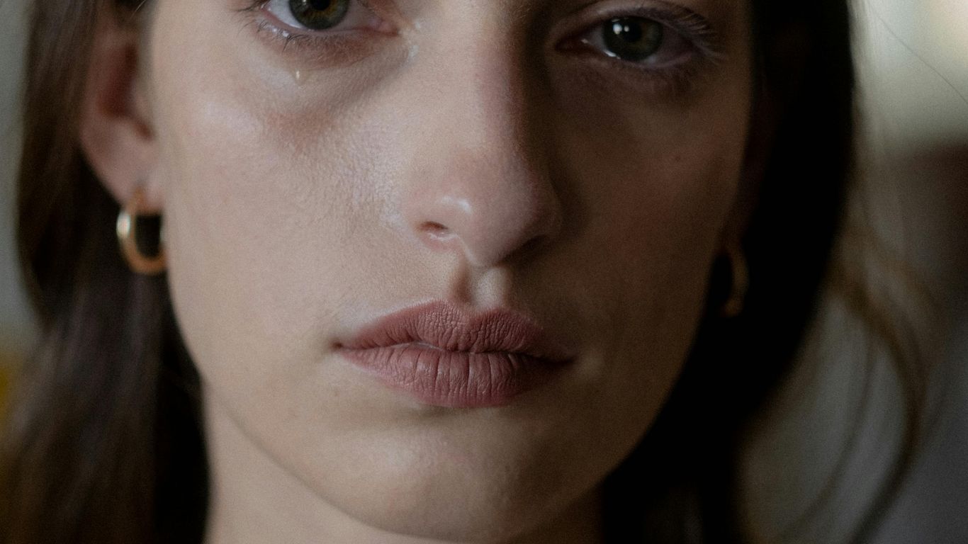 Close-up of a person with neutral expression, wearing earrings.