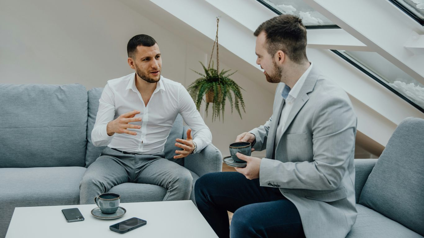 two men sitting on a couch talking to each other