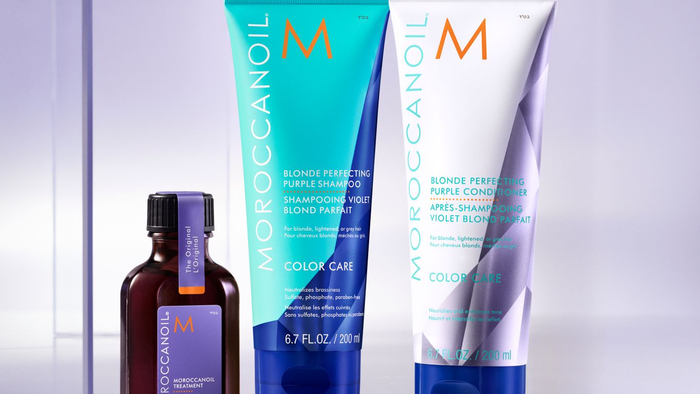 Moroccanoil haircare products on reflective surface with purple backdrop.