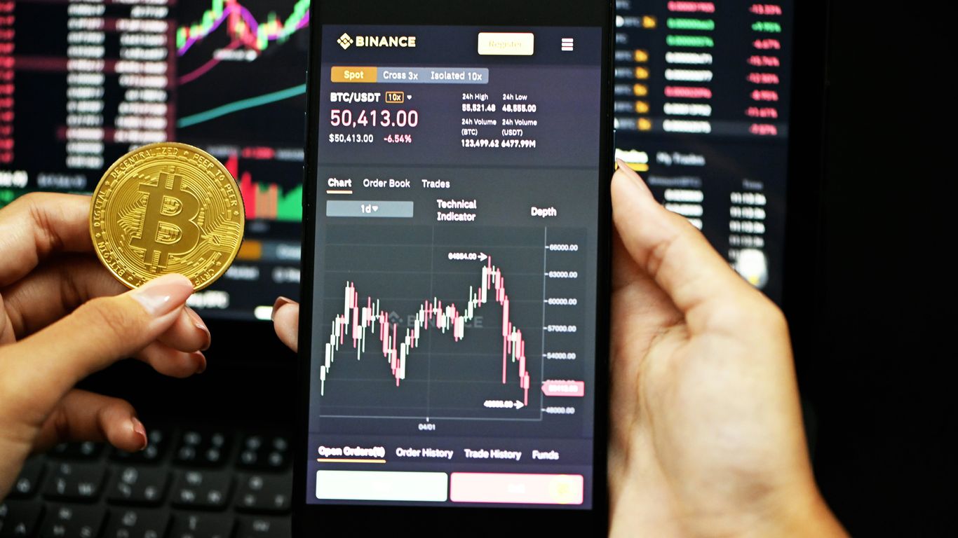 A person holds a phone displaying cryptocurrency market data.