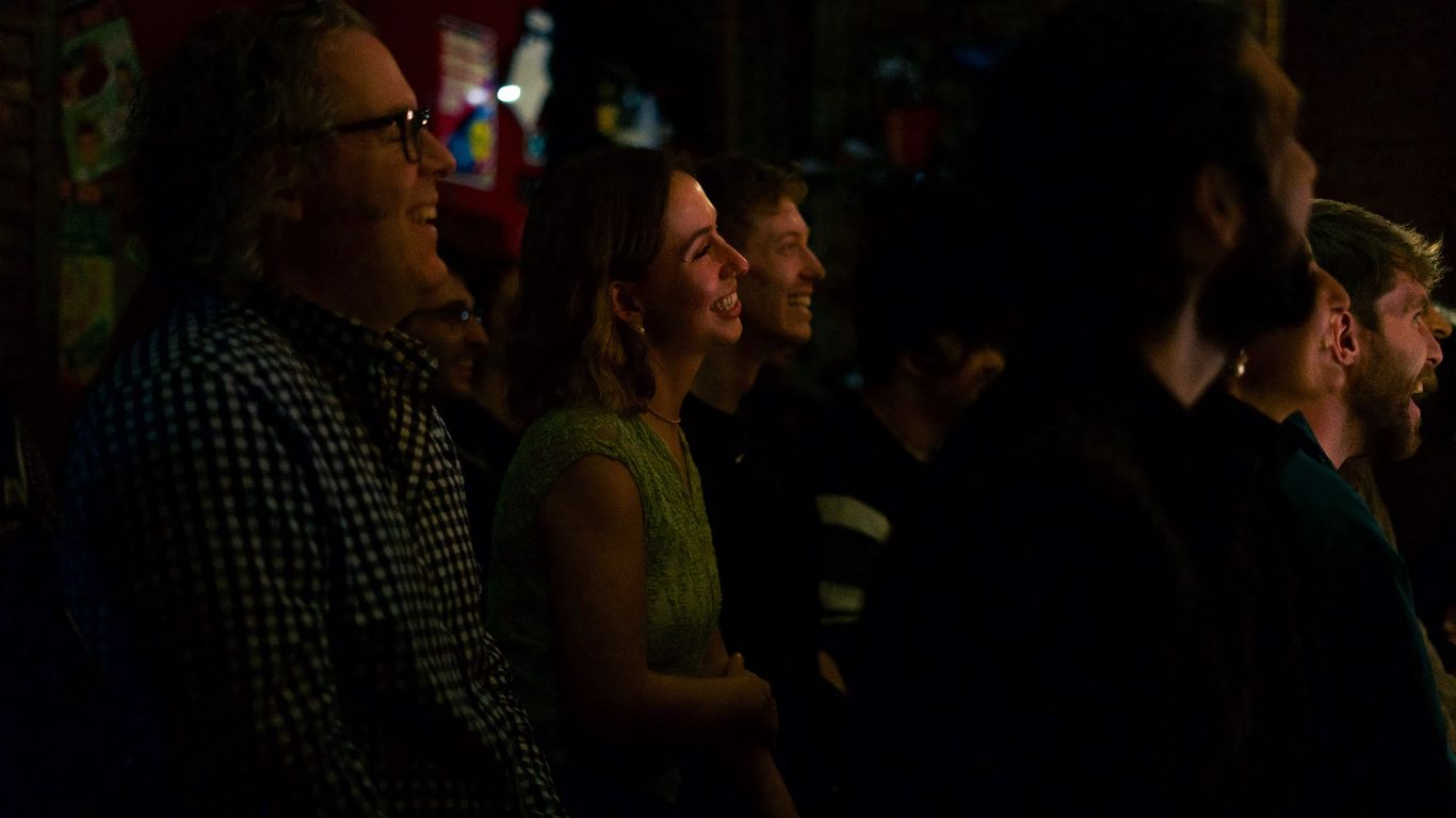A group of people are seated and laughing in a dimly lit room.