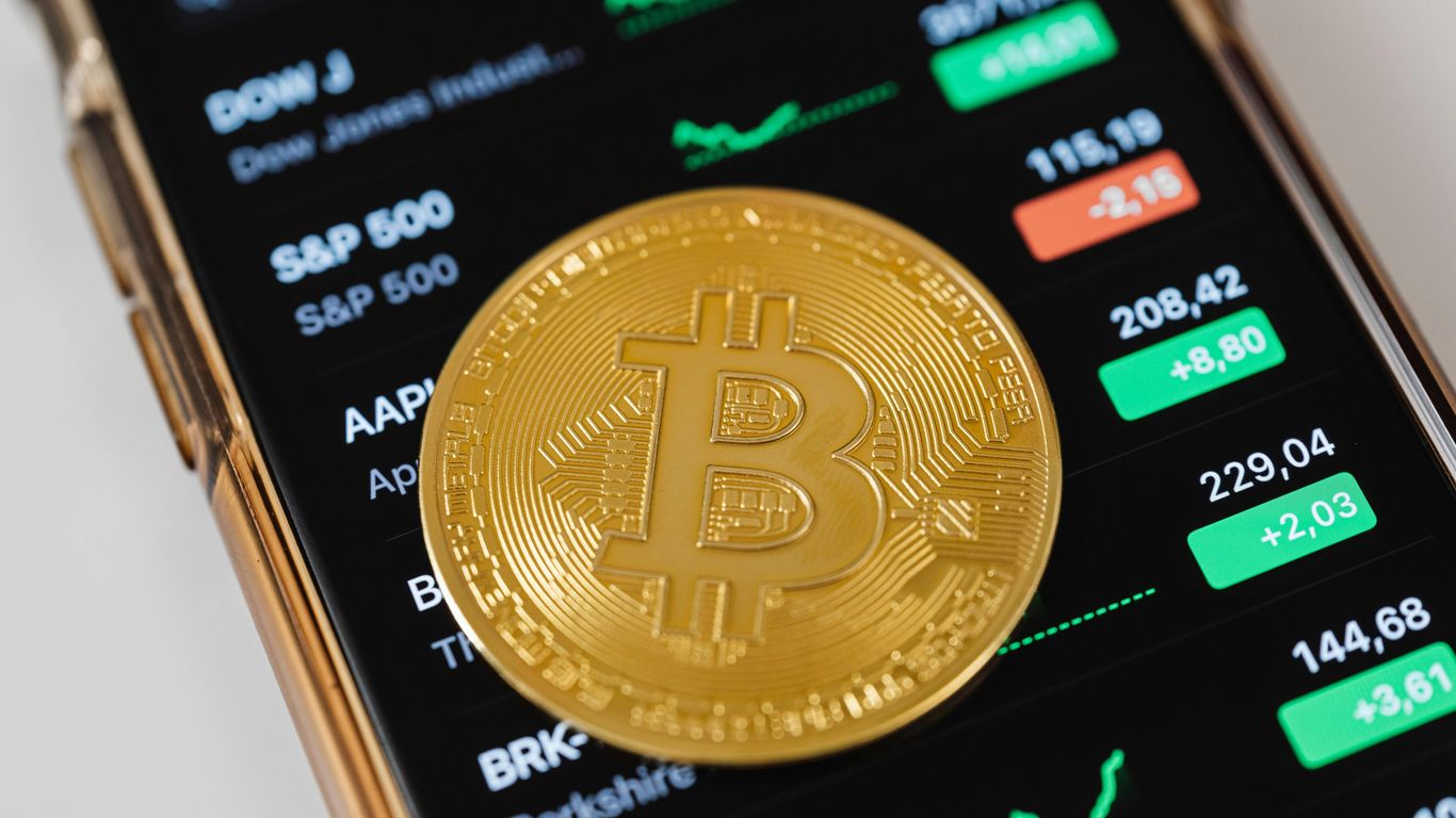 Bitcoin coin on a smartphone displaying stock market data.