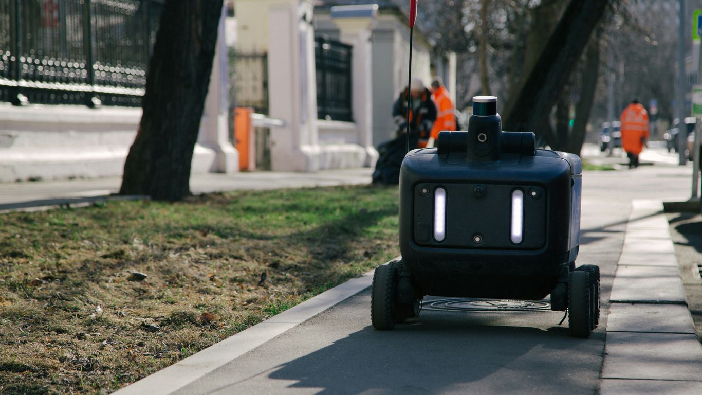 Robot delivery vehicle moves down a city sidewalk.