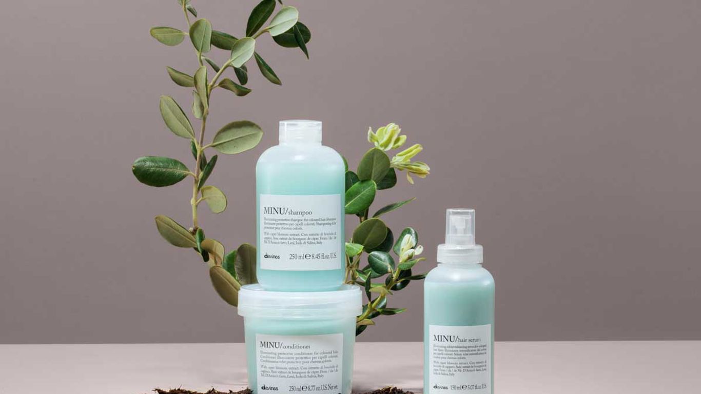 Bottles of haircare products with plants on a neutral background.