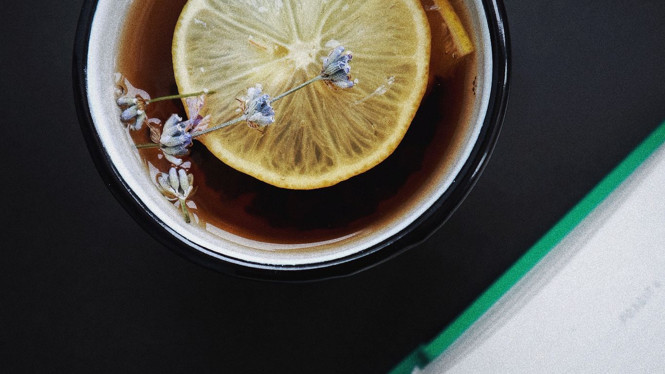 Cup of tea with lemon, flowers, and open book nearby.