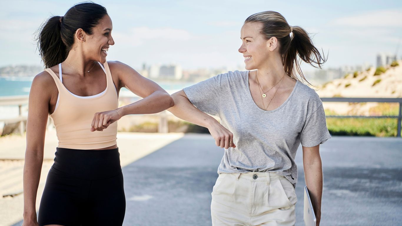 woman in gray shirt elbow bumping with woman in sports outfit