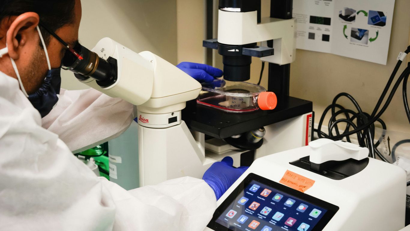 a man in white lab coat looking through a microscope