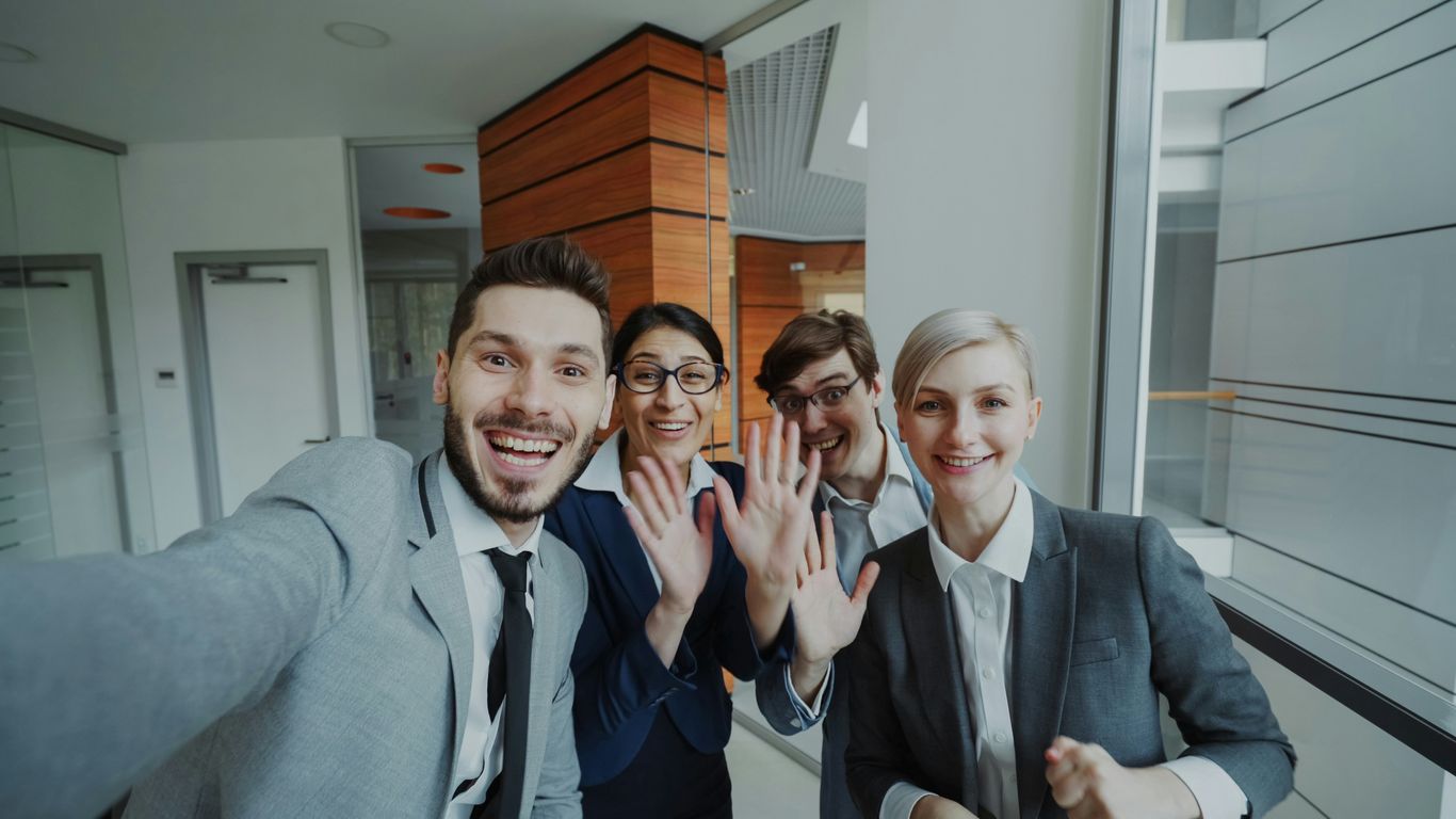 Four business people smiling and waving at camera.