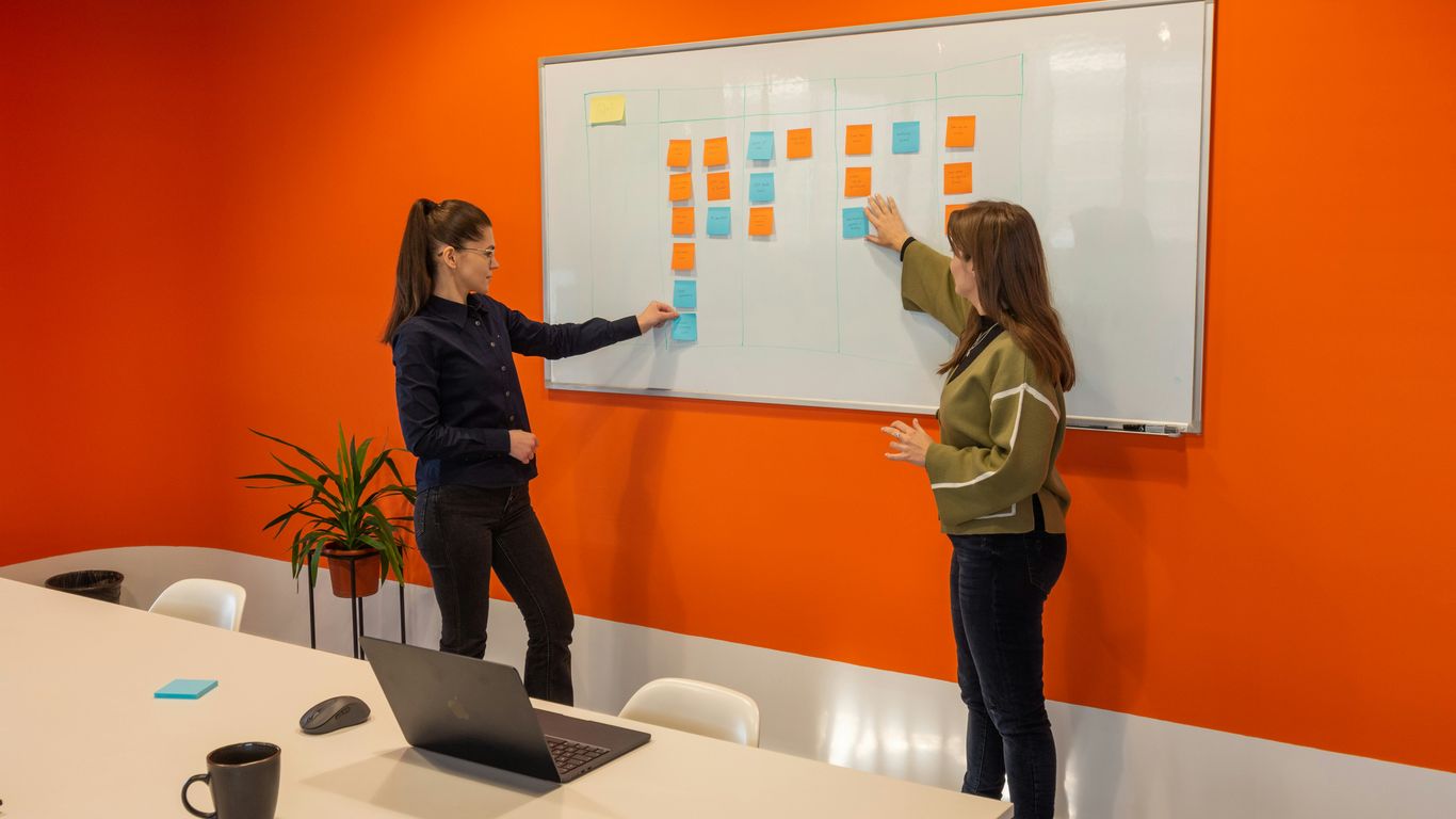 two women standing in front of a white board