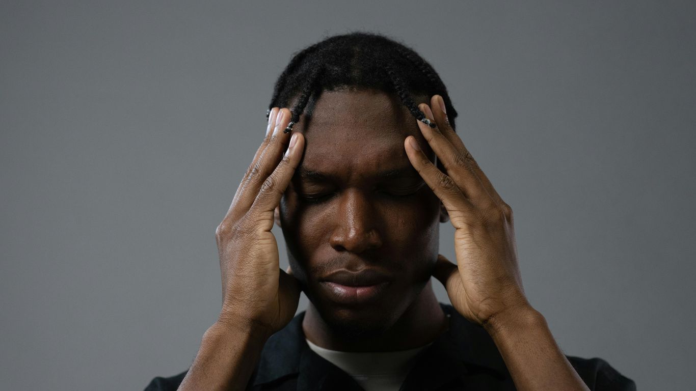 Person with hands on temples, eyes closed, appearing stressed or thoughtful.