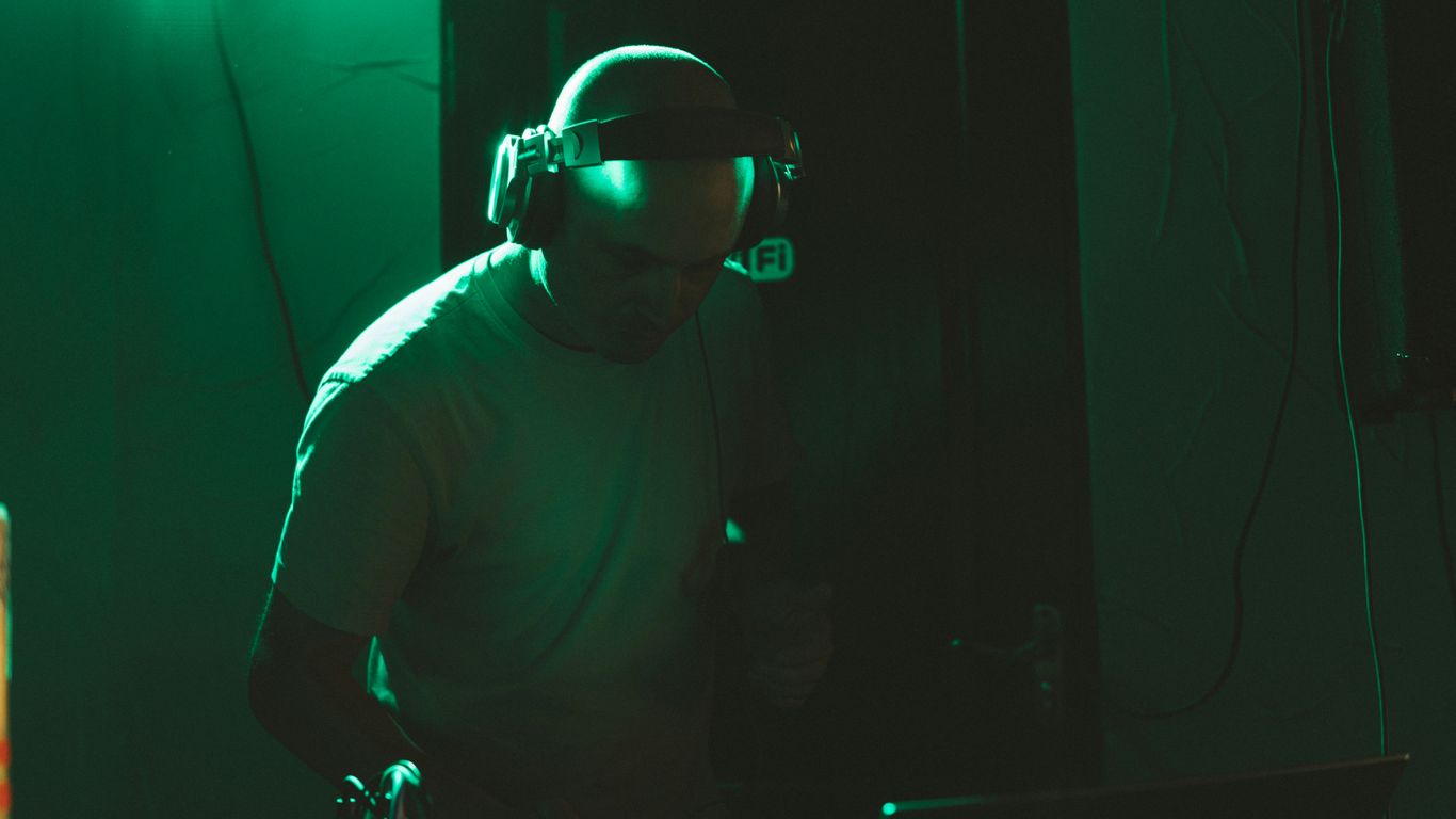 Dj wearing headphones plays music in a green lit room