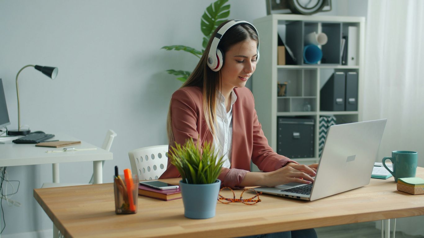 Young woman wearing headphones works on laptop at desk.