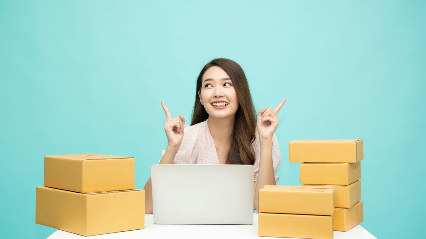 a woman sitting at a table with a laptop surrounded by boxes