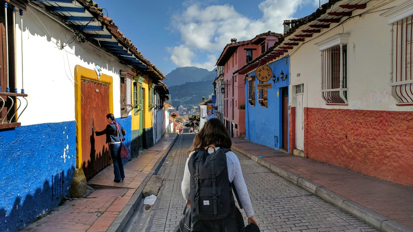 person in gray shirt with backpack walking on street between houses