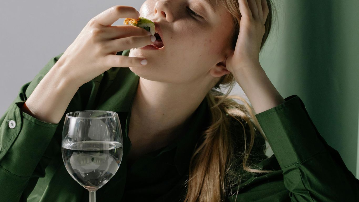 Person in green shirt eating sushi, glass of water nearby.