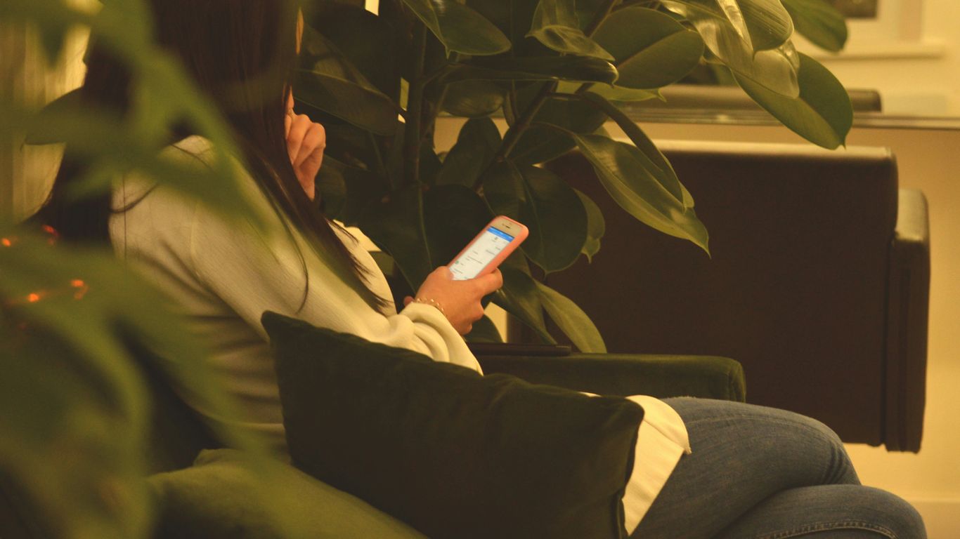 person using smartphone while sitting on black sofa between green plants