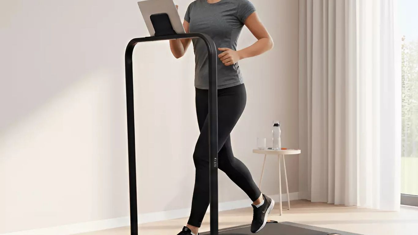 A person runs on a treadmill while looking at a tablet.