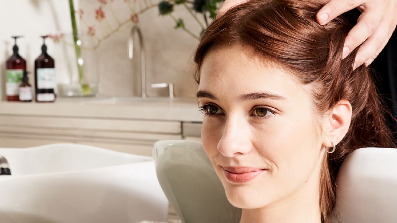 Person smiling, getting a scalp massage at a hair salon.