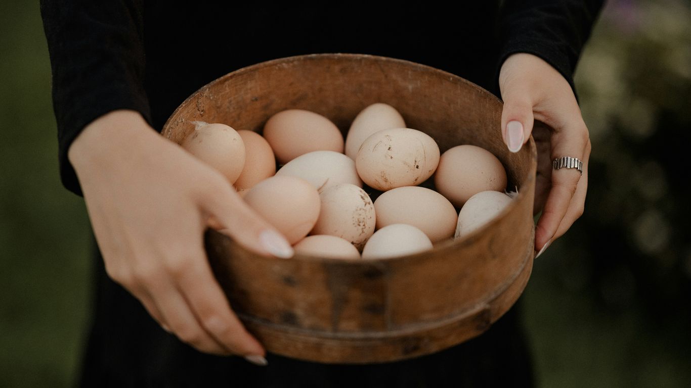 a woman holding a wooden bowl filled with eggs