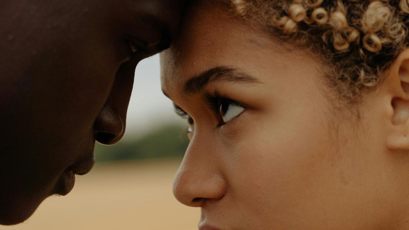 Two people touch foreheads, gazing intently at each other.